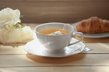 Cup of tea with croissant and flowers on table