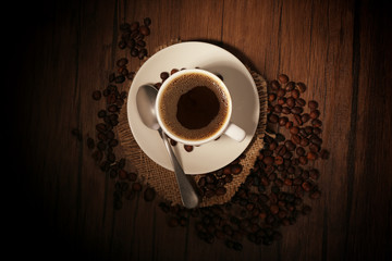 Cup of coffee with beans and spoon on wooden background