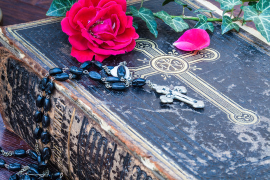 Nahaufnahme einer antiken Bibel mit Rosenkranz und Rose