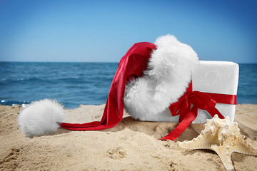 Gift box with Santa hat and sea star on beach. Christmas holiday concept