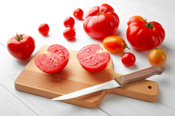 Composition of tomatoes, knife and cutting board on white wooden background