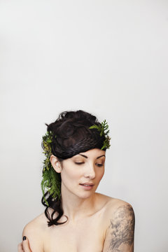 Sensuous young woman wearing leaves in hair against white background