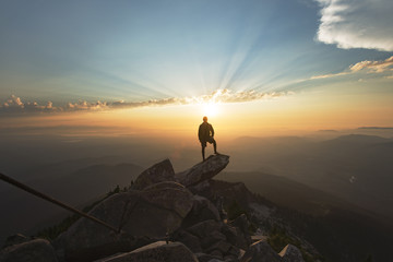 Man standing on rock at cliff against sky during sunset