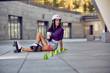 Teenager on rollerblading sitting on street and drink coffee at sunny day. Active lifestyle. Happy...