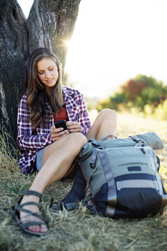 Young woman using mobile phone while sitting with backpack on grassy field