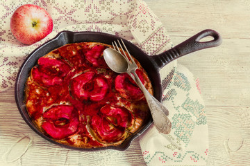 Homemade apple pie in black cast-iron pan on wooden background and fruits. The cake is decorated with round slices of apples. Toned photo