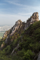 Fototapeta na wymiar View of the city far away from above and steep granite peaks of Jaunbong Peak on Dobongsan Mountain at the Bukhansan National Park in Seoul, South Korea.
