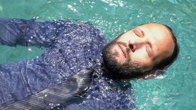 Businessman with closed eyes floating on water in pool, super slow motion 240fps
