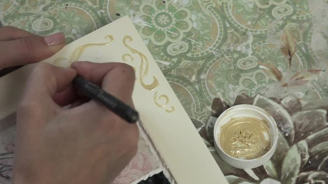 The girl draws ornament gold paint on a wooden frame