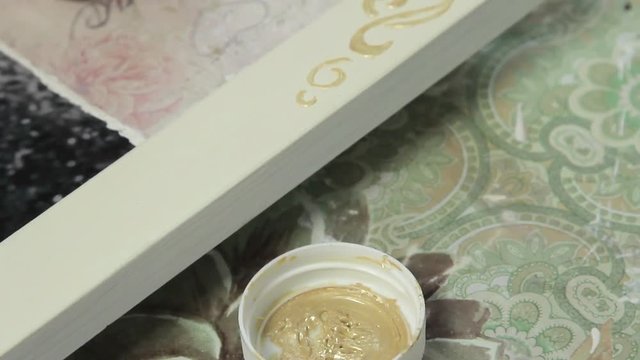 The girl draws ornament gold paint on a wooden frame