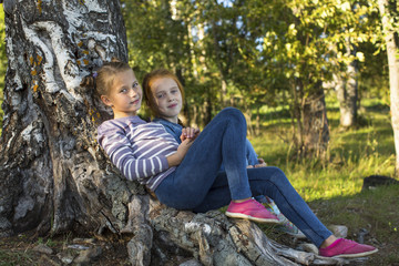 Two little girl sitting on the roots of a tree.