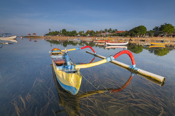 Traditional Balinese ships Jukung in Sanur beach at sunrise, Bali, Indonesia at blue sky