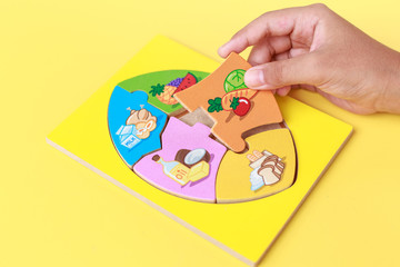 Obraz premium Hand of kid holding wooden jigsaw of the 5 food Groups. Child de