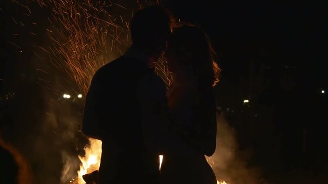 Silhouette of an embracing happy couple standing near campfire