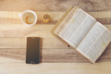 A mobile phone with a cup of coffee, cookies, old dictionary on a wooden floor.