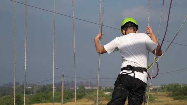 Teenager walking on sticks tied with ropes Rope park. On youth helmet and safety belt