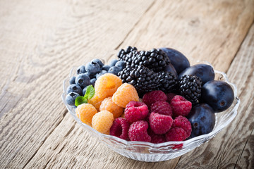 Fresh summer berries and fruits in  glass bowl on wooden rustic