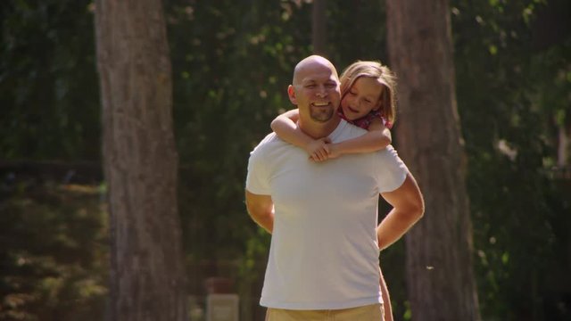Slow motion dad giving daughter a piggy back ride in the park