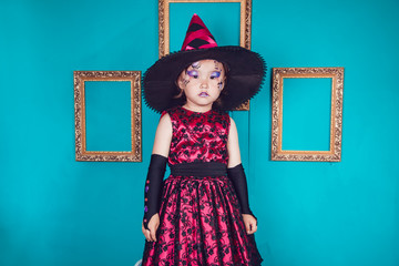 Fototapeta premium Little girl in the witch costume on a background of turquoise wall