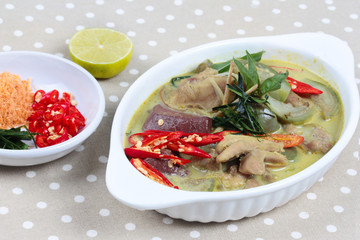 Green chicken curry in coconut milk served with side dish as minced dried shrimp,sliced red chili,sliced kaffir lime leaves and green lemon.on gray.Selective focus.