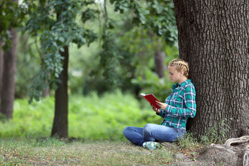 Young woman reading book sitting near a tree