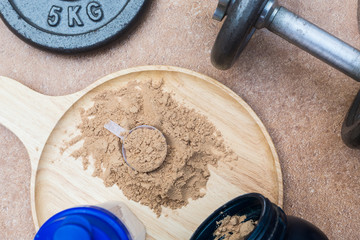 Scoop of whey protein on a wooden plate with jar. on top view