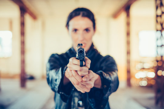 Young woman with gun aiming at camera