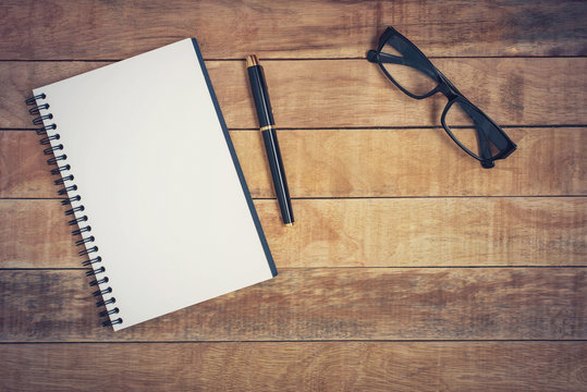 Glasses and notebook with pen placed on a wooden table