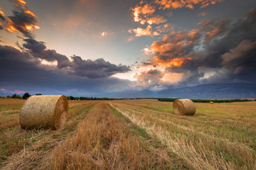 Sunset over farm field with hay bales.