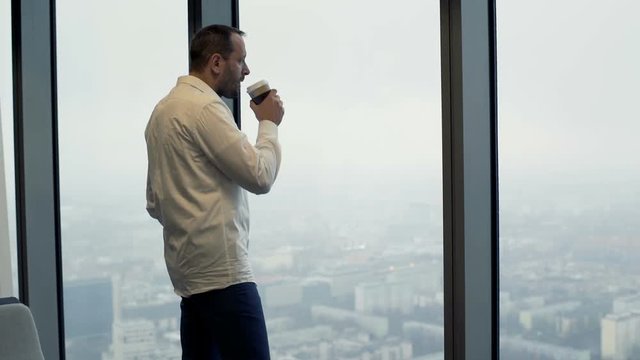 Young businessman drinking coffee and looking through tke window 
