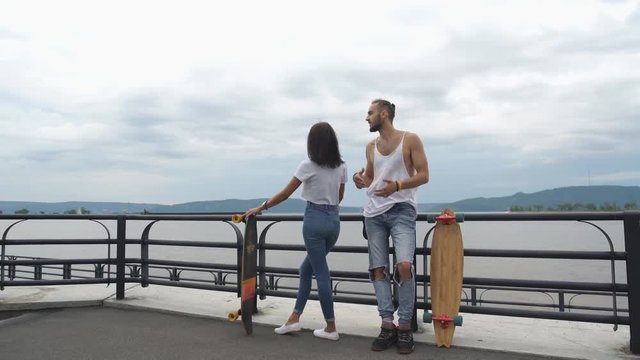 Beautiful guy with the girl on long boards talking to on the waterfront