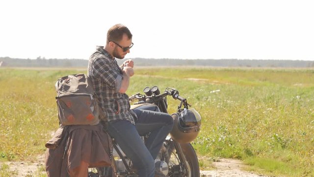 Stylish man smoking on the vintage custom cafe racer in a field.