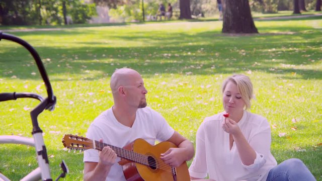 Man serenades woman with guitar in the park