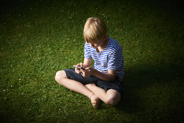 Fototapeta premium Child young boy with mobile phone outdoor. Child looking at the screen, playing, using apps. Boy playing with smartphone.