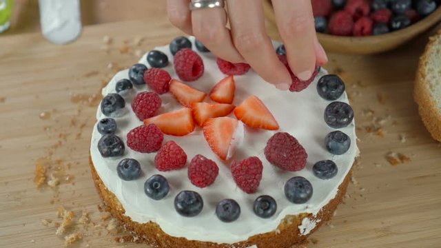Woman cooking berry cake and decorating biscuit with raspberries