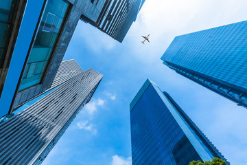 Skyscrapers with a flying airplane against blue sky.
