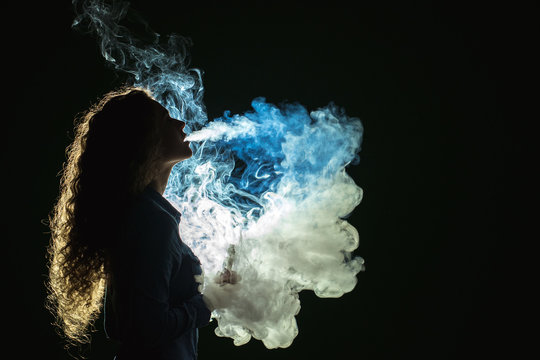 The girl smoke electronic cigarette on the dark background