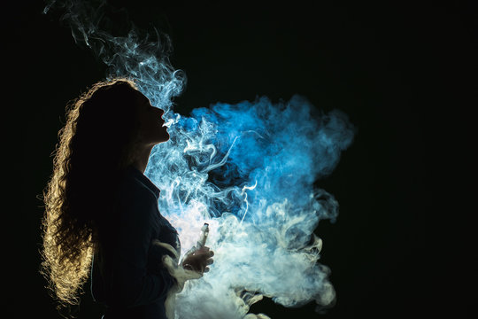 The girl smoke electronic cigarette on the dark background