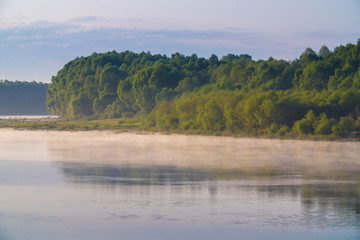 The picturesque water surface with fog and steam near the forest