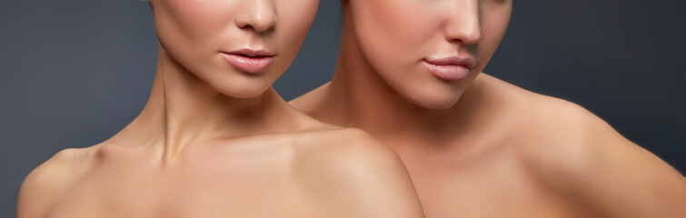 Close-up lips and shoulders of two younh girls with perfect skin over grey background