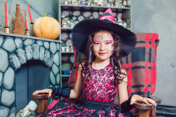 Girl in a witch costume sitting on a chair in the Halloween decorations