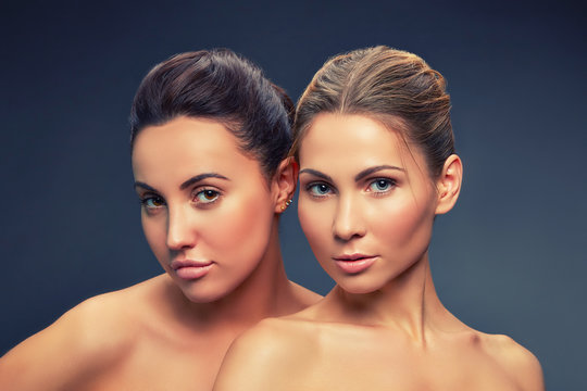Portrait of two young girl with perfect toned skin and natral make-up over grey background