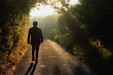 Alone man walking along a small country road in a misty morning