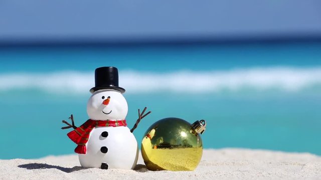 Snowman toy and christmas decoration ball at sandy beach on Caribbean sea background. New Year celebration
