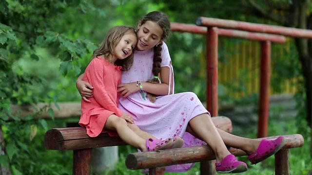 Two girls sits on a wooden bench and embrace. Sisters sits together, communicates and embrace