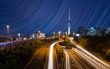 Fototapeta na wymiar City skyline with traffic on highway and star trails on sky, Auckland