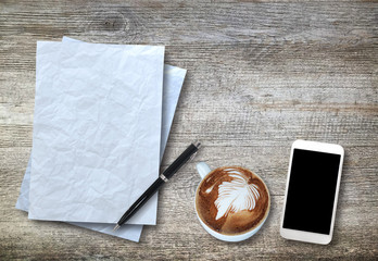 Top view of white paper, smartphone, pen and cup of coffee on wo