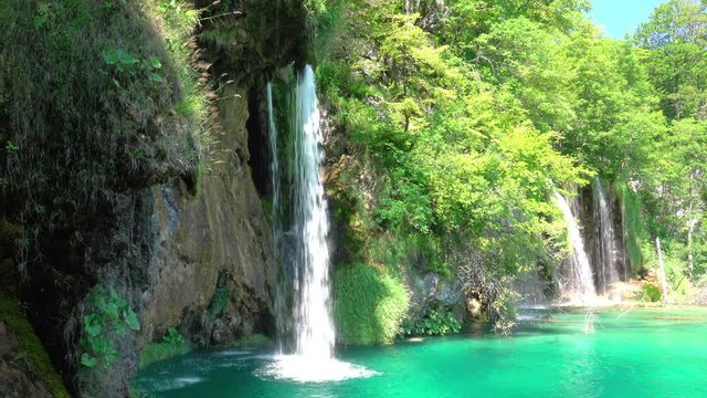 Summer. Sunny weather. Forest lake. Several beautiful waterfalls on grassy rock. UHD