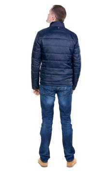 Back view of handsome man in blue windcheater looking. Standing young guy in jeans. Rear view people collection.  backside view of person.  Isolated over white background.
