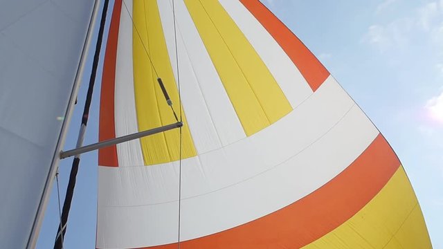 Multicolored Sailing in the wind through the waves. Full sails, very strong wind. Ocean race, real adventure. Real spray. Sun sails, and adventure. Sail blows in the wind on a boat. Slow motion shot.